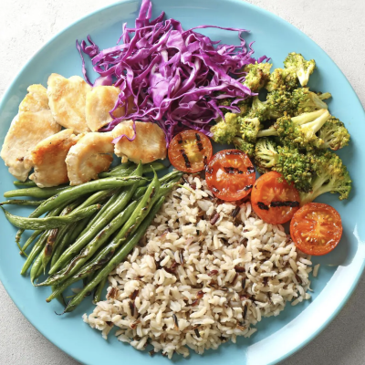 Blue plate with plant based foods rice, asparagus, purple cabbage, tomato, broccoli