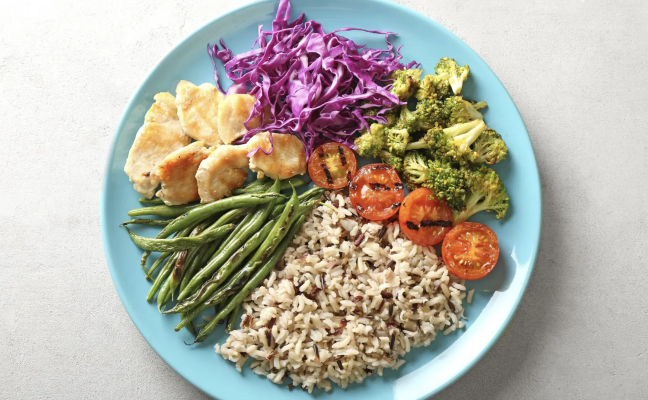 Blue plate with plant based foods rice, asparagus, purple cabbage, tomato, broccoli