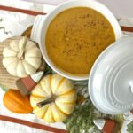 butternut squash soup in white bowl overhead shot next to mini pumpkins on autumn table runner