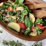 Maple Bliss salad with apple slices, lettuce, farro and herbs in wood bowl with serving utensils