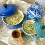 two pots of potato leek soup between a blue vase and wooden measuring cup