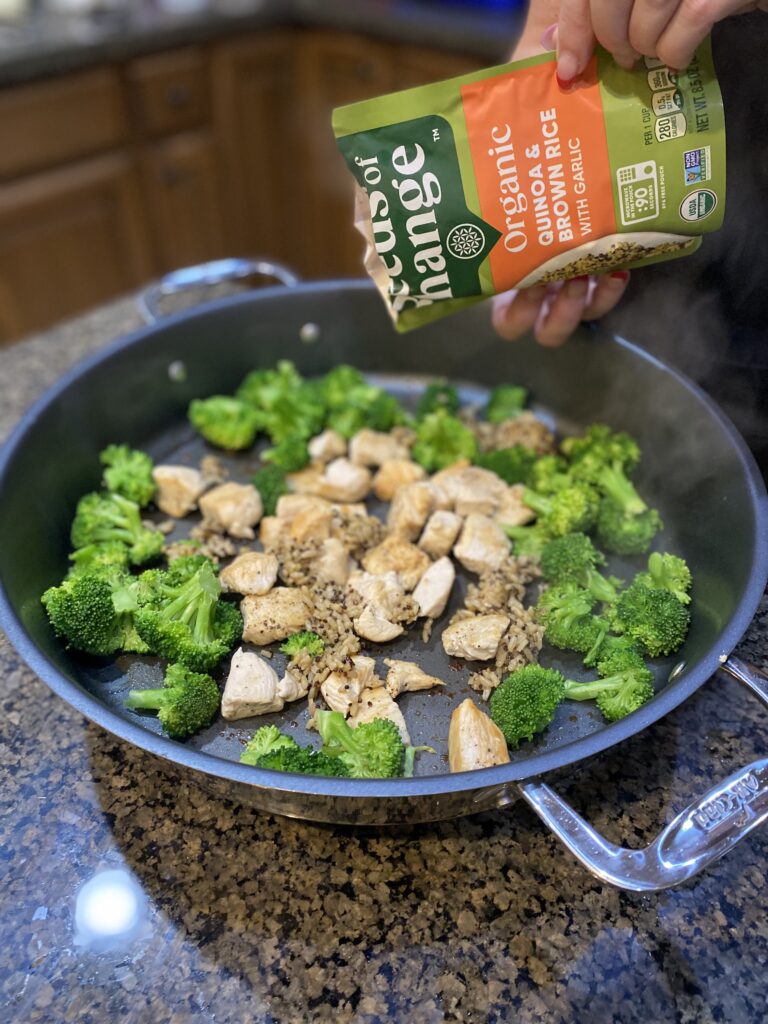 meal cooking with broccoli on outer border of the electric grill pan, chicken cooked center and pouring in seeds of change quinoa mix