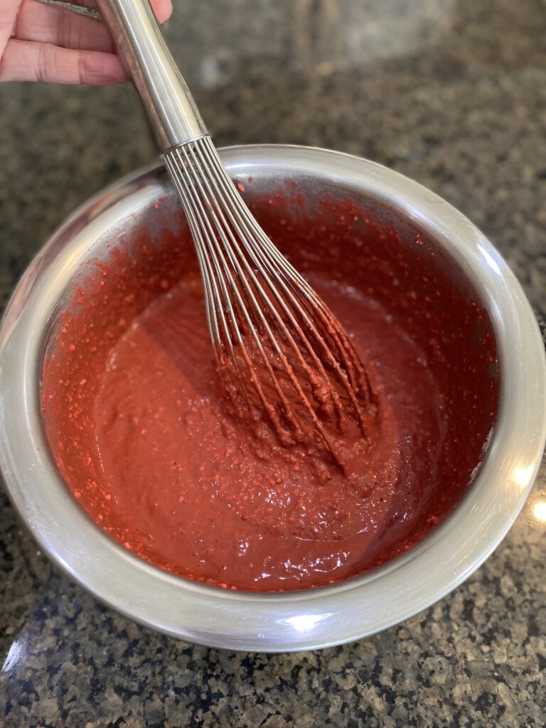 fully mixed wet and dry ingredients, red in color in metal bowl with whisk