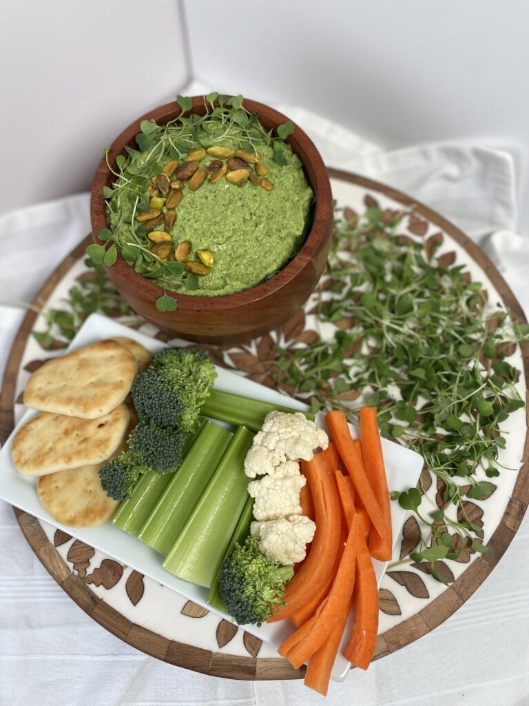 green goddess hummus on circular serving tray with pita bread and raw veggies for dipping