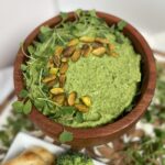Green goddess hummus in wood bowl with pistachio and herb garnish on top