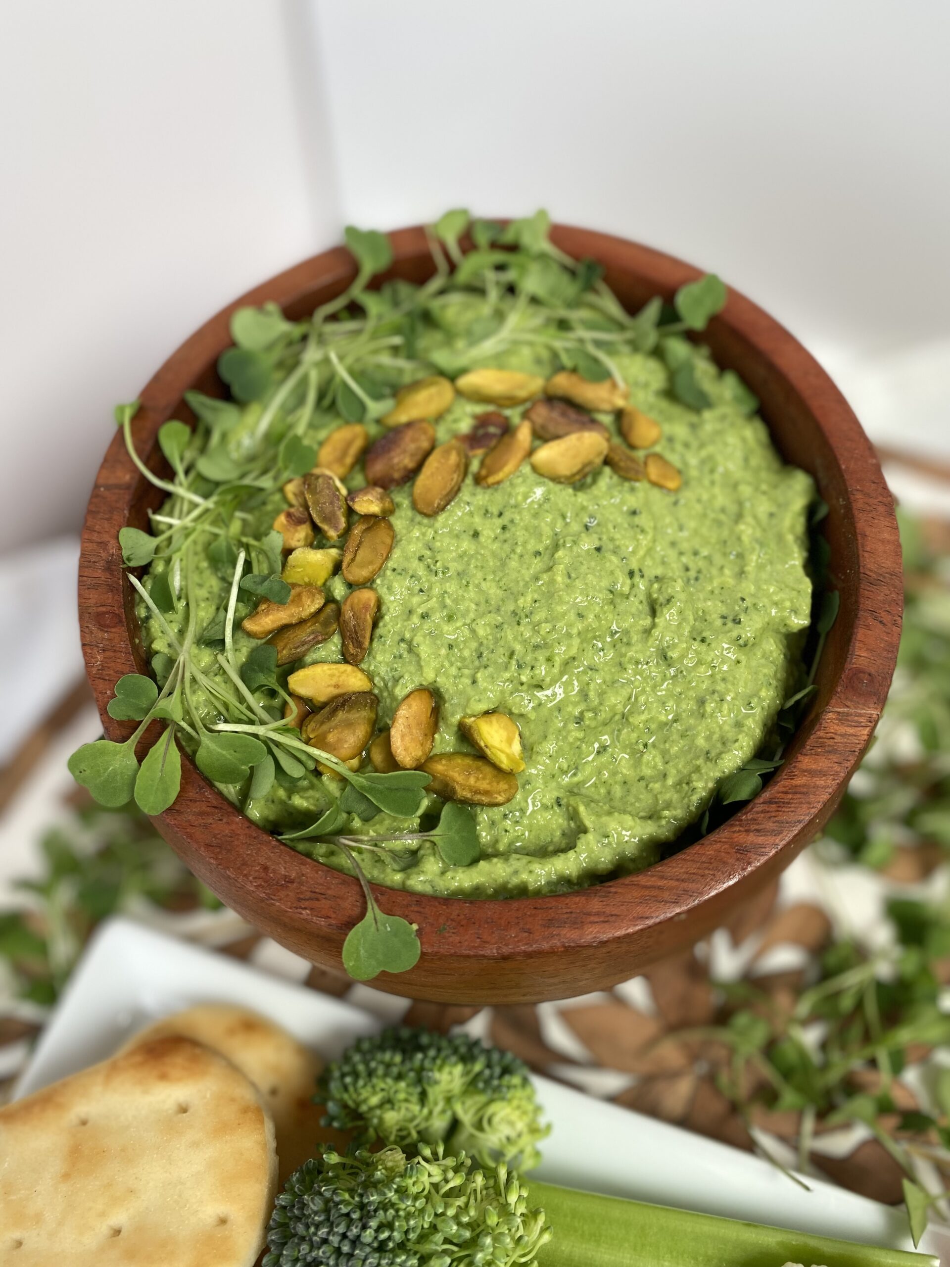 Green goddess hummus in wood bowl with pistachio and herb garnish on top