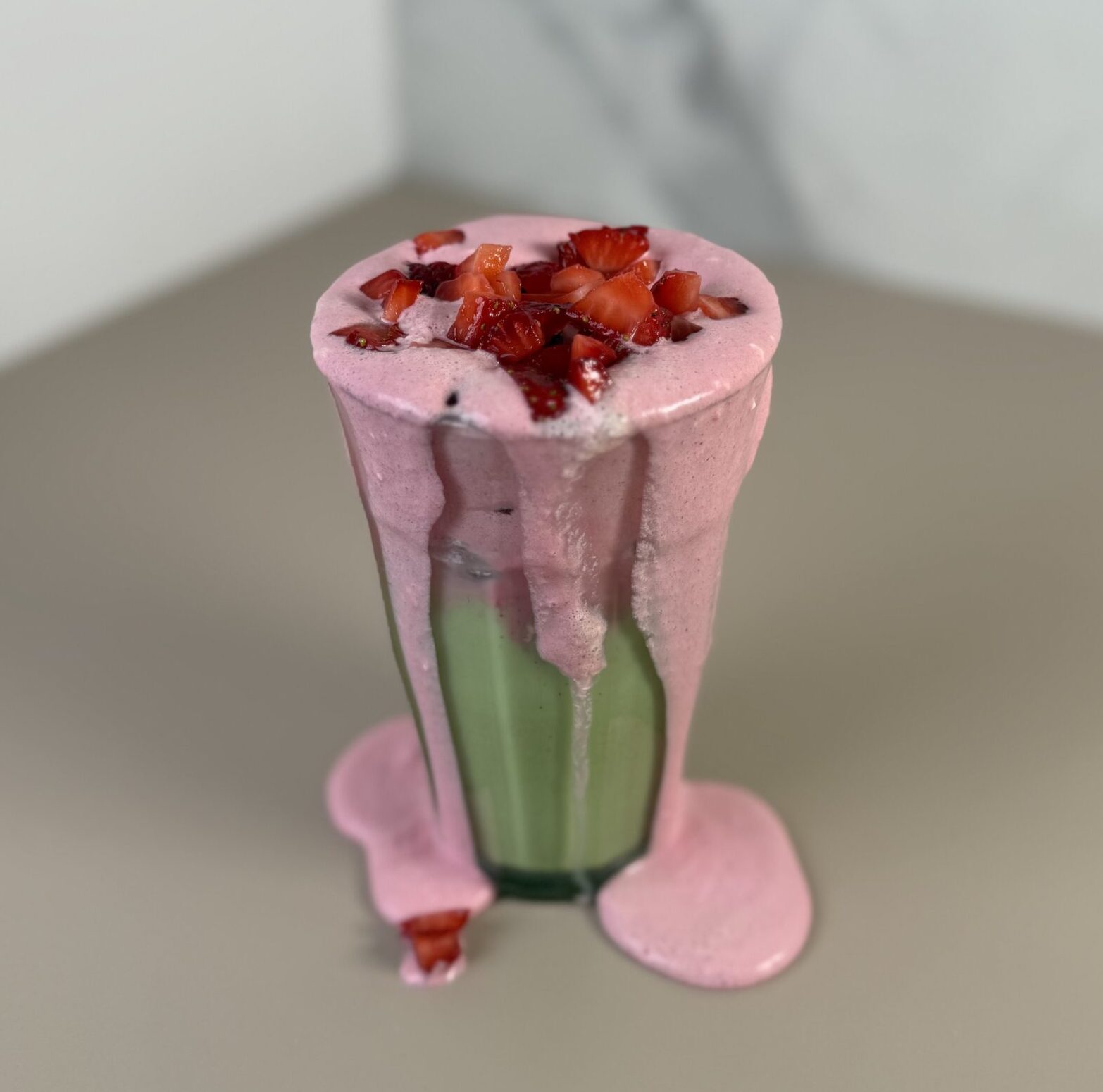 Iced Strawberry Matcha dripping out of a clear glass with diced strawberries on top