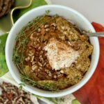 Pumpkin spice oatmeal in white bowl with garnish of Greek yogurt dollop and curved garnish of thyme, chopped pecans and cinnamon sprinkle