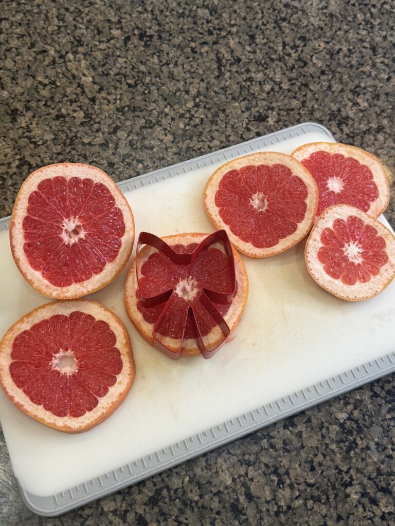 slices of grapefruit on cutting board. one of the grapefruit slices has a gift bow cookie cutter on top