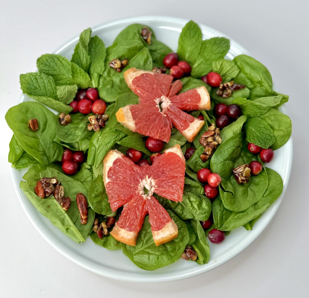 spinach salad with two grapefruit slices in bow shapes, cranberries and candied pecans on white plate