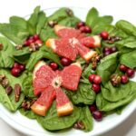 spinach salad with two grapefruit slices in bow shapes, cranberries and candied pecans on white plate