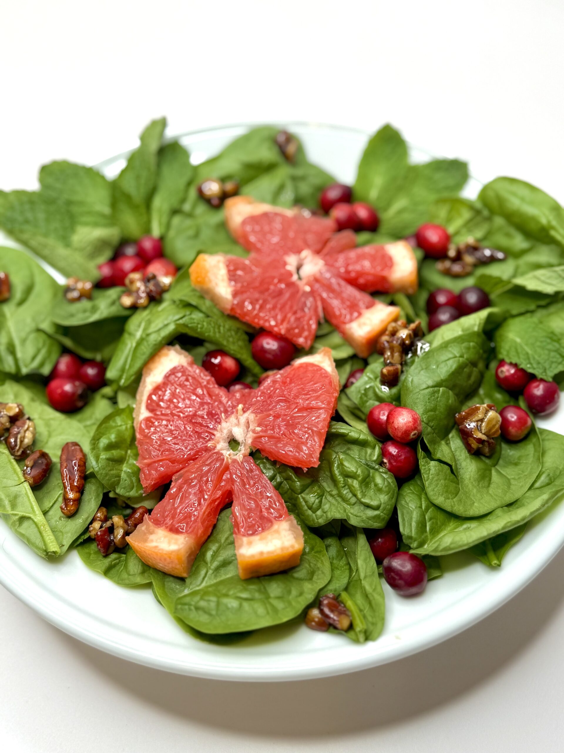 spinach salad with two grapefruit slices in bow shapes, cranberries and candied pecans on white plate