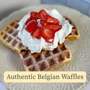 Authentic Belgian Waffles cover image with white plate, 3 Belgian waffles on it topped with whipped cream and sliced strawberries.