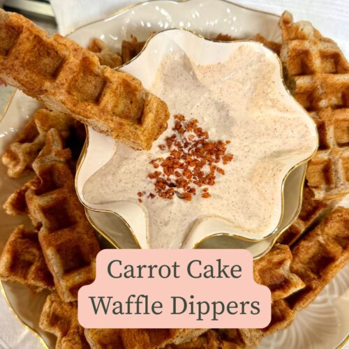 bowl of cinnamon, greek yogurt and cream cheese dip with carrot cake waffle sticks around it with one about to dip in