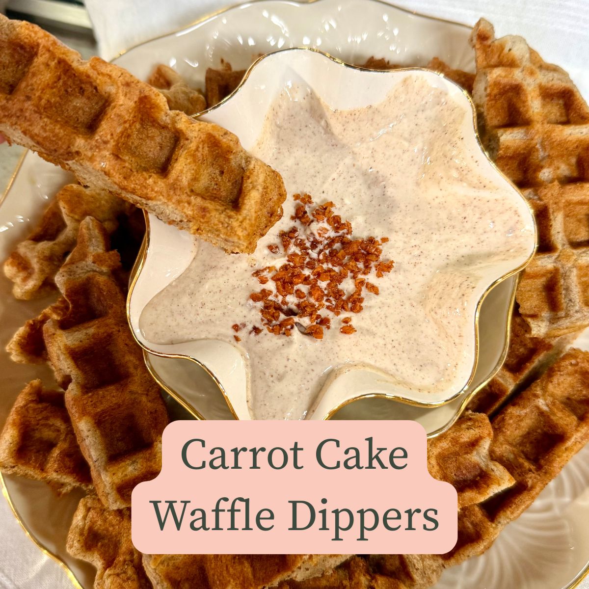 bowl of cinnamon, greek yogurt and cream cheese dip with carrot cake waffle sticks around it with one about to dip in